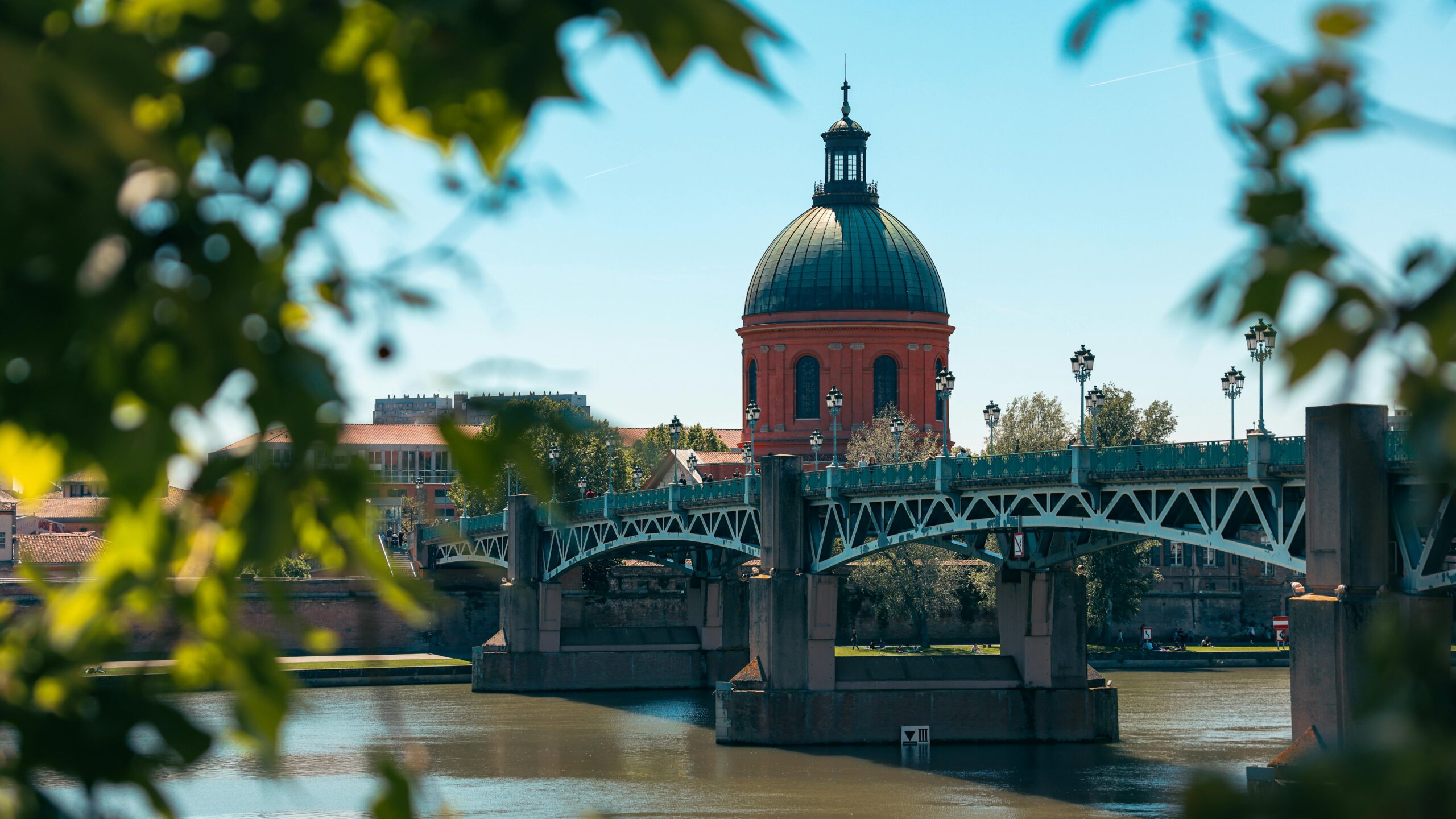 Scenic view of Pont Saint-Pierre and red dome in Toulouse, France framed by leaves.